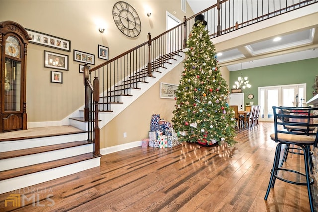 stairs with a towering ceiling, coffered ceiling, hardwood / wood-style floors, and a chandelier