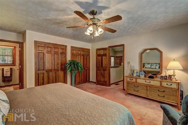 carpeted bedroom with ceiling fan, two closets, and a textured ceiling