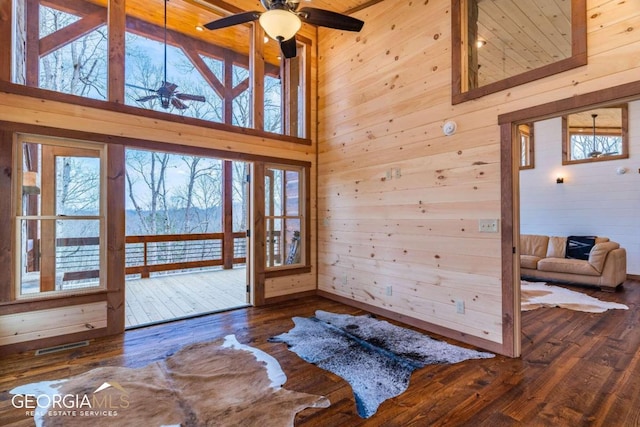 interior space featuring wood walls, dark hardwood / wood-style flooring, ceiling fan, and a high ceiling