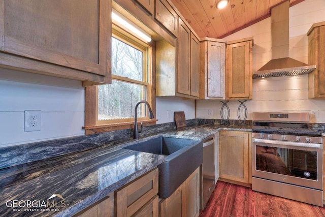 kitchen featuring appliances with stainless steel finishes, dark stone countertops, vaulted ceiling, dark wood-type flooring, and wall chimney range hood