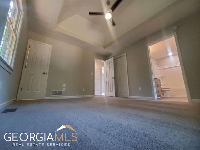 empty room featuring a raised ceiling, ceiling fan, and dark carpet