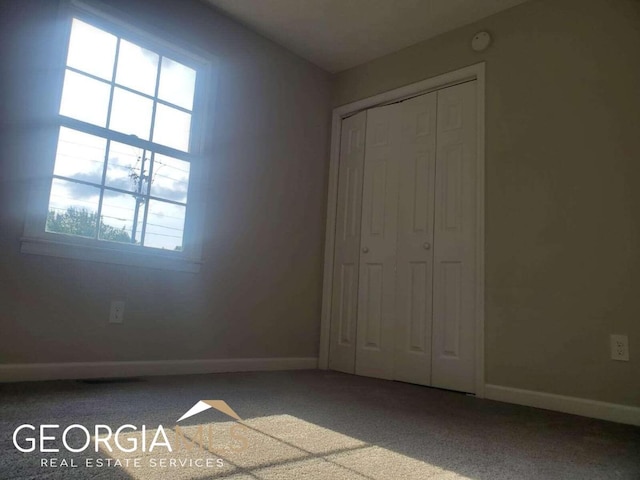 unfurnished bedroom with a closet, dark colored carpet, and multiple windows