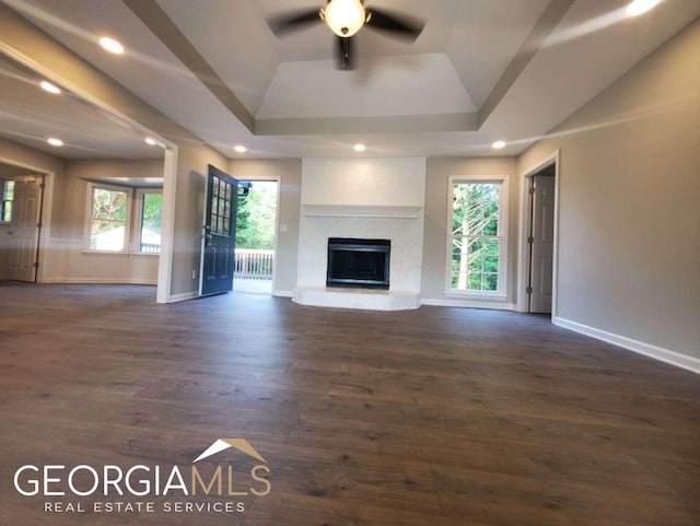 unfurnished living room featuring ceiling fan, dark wood-type flooring, a tray ceiling, and a large fireplace