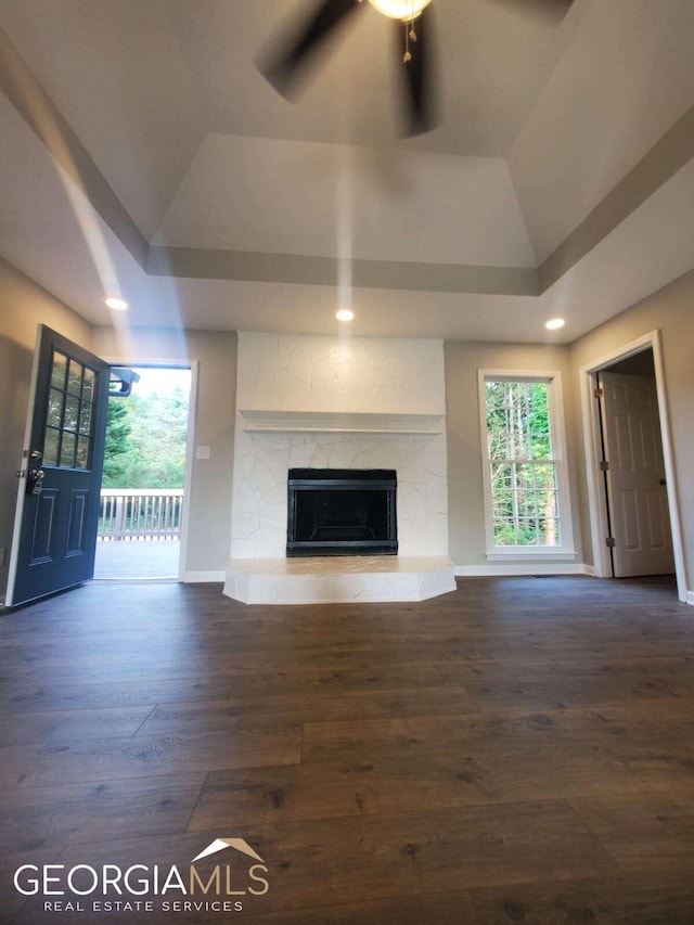 unfurnished living room with dark hardwood / wood-style flooring, ceiling fan, a fireplace, and a tray ceiling