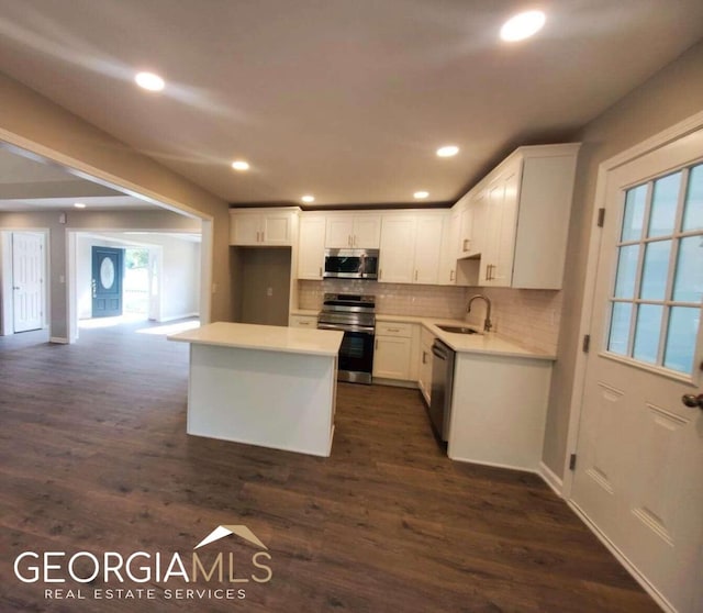 kitchen with appliances with stainless steel finishes, a kitchen island, sink, white cabinetry, and dark hardwood / wood-style floors