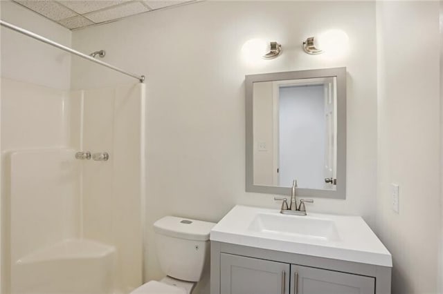 bathroom with walk in shower, a paneled ceiling, toilet, and vanity