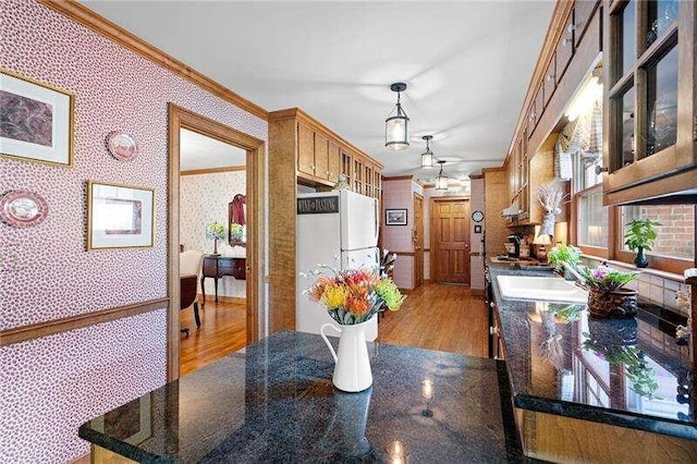 kitchen with light hardwood / wood-style floors, pendant lighting, dark stone countertops, sink, and ornamental molding