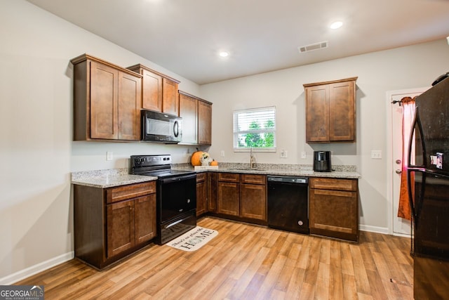 kitchen with light stone counters, sink, light hardwood / wood-style flooring, and black appliances