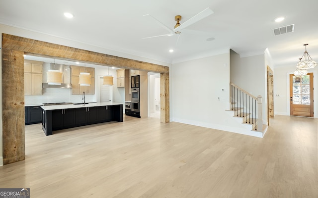 kitchen with hardwood / wood-style flooring, hanging light fixtures, a center island with sink, and wall chimney range hood