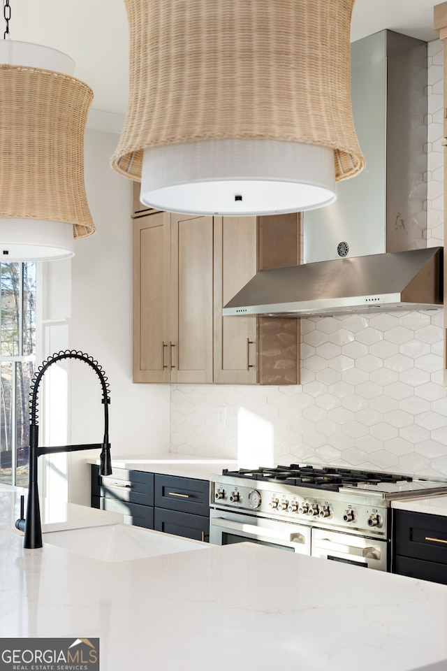 kitchen with light brown cabinetry, stainless steel stove, light stone countertops, decorative backsplash, and wall chimney range hood