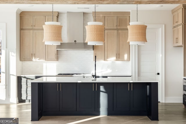 kitchen with tasteful backsplash, wall chimney exhaust hood, an island with sink, and hanging light fixtures