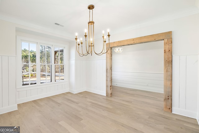 unfurnished dining area featuring a notable chandelier, ornamental molding, and light hardwood / wood-style floors