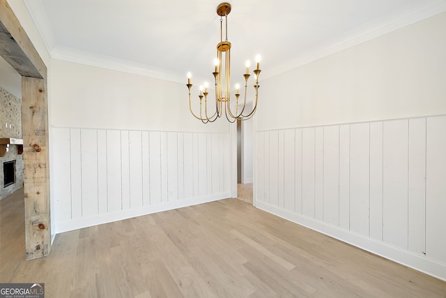 unfurnished dining area featuring an inviting chandelier, a fireplace, ornamental molding, and wood-type flooring