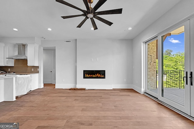 kitchen featuring ceiling fan, light hardwood / wood-style floors, wall chimney range hood, tasteful backsplash, and white cabinetry