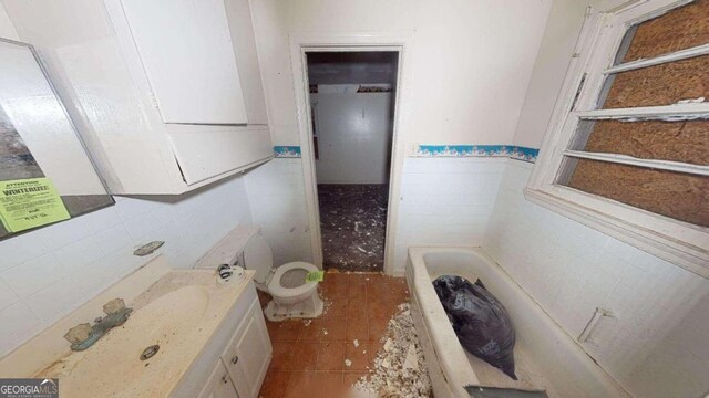 bathroom with a bathing tub, vanity, tile walls, and toilet
