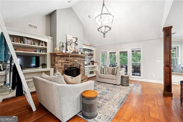 living room with a fireplace, french doors, high vaulted ceiling, hardwood / wood-style flooring, and a notable chandelier