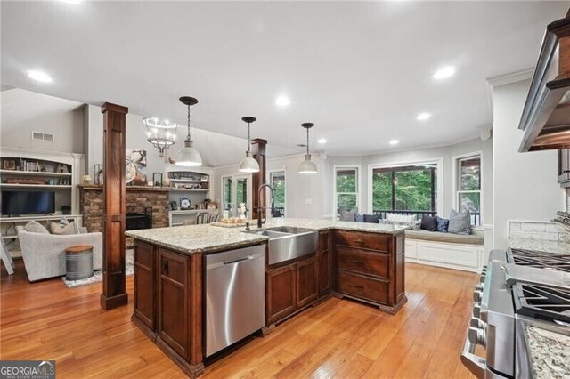 kitchen with appliances with stainless steel finishes, light hardwood / wood-style flooring, a center island with sink, sink, and pendant lighting