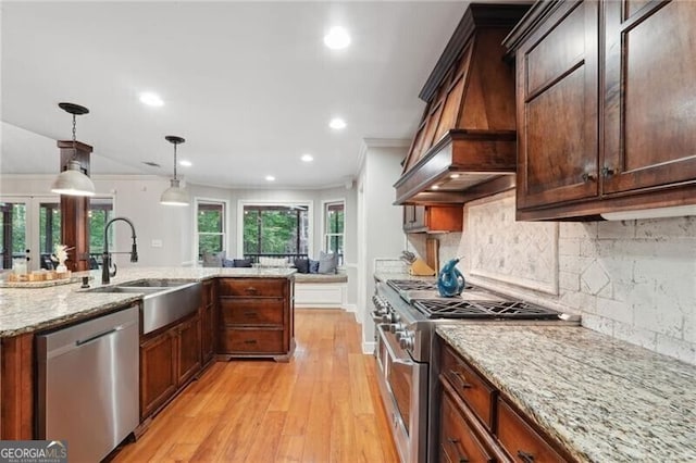 kitchen with custom range hood, light hardwood / wood-style flooring, hanging light fixtures, appliances with stainless steel finishes, and ornamental molding