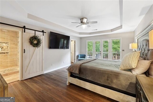 bedroom with wood-type flooring, ceiling fan, a tray ceiling, ensuite bath, and a barn door