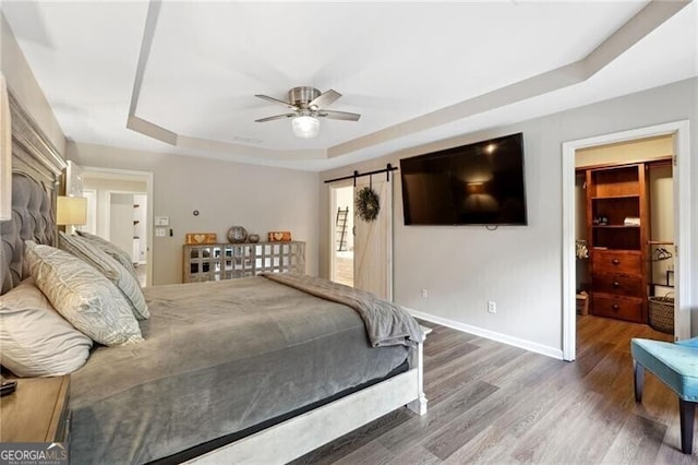 bedroom with hardwood / wood-style flooring, a raised ceiling, a barn door, and ceiling fan