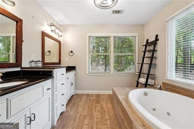 bathroom with vanity, a healthy amount of sunlight, hardwood / wood-style floors, and a relaxing tiled tub