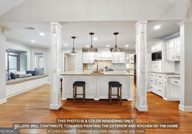 kitchen with decorative columns, light wood-type flooring, premium range hood, decorative backsplash, and a kitchen bar