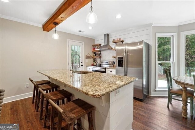 kitchen with wall chimney range hood, a kitchen island with sink, dark hardwood / wood-style floors, hanging light fixtures, and appliances with stainless steel finishes