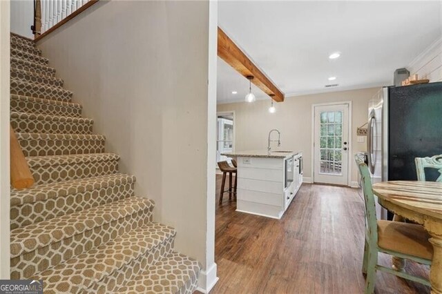 stairs with beamed ceiling, sink, and dark wood-type flooring