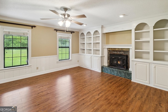 unfurnished living room featuring built in features, a premium fireplace, ceiling fan, a textured ceiling, and dark wood-type flooring