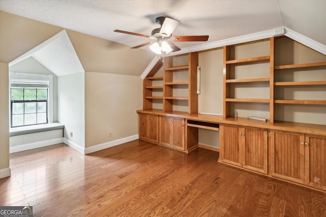 unfurnished office featuring lofted ceiling, ceiling fan, light wood-type flooring, and a textured ceiling