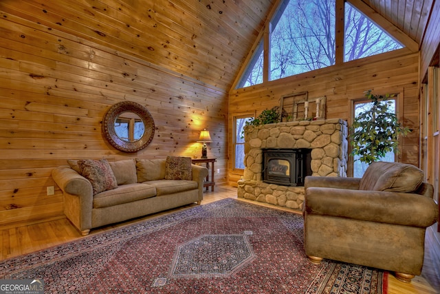 living room featuring light hardwood / wood-style flooring, a stone fireplace, wood ceiling, high vaulted ceiling, and wooden walls