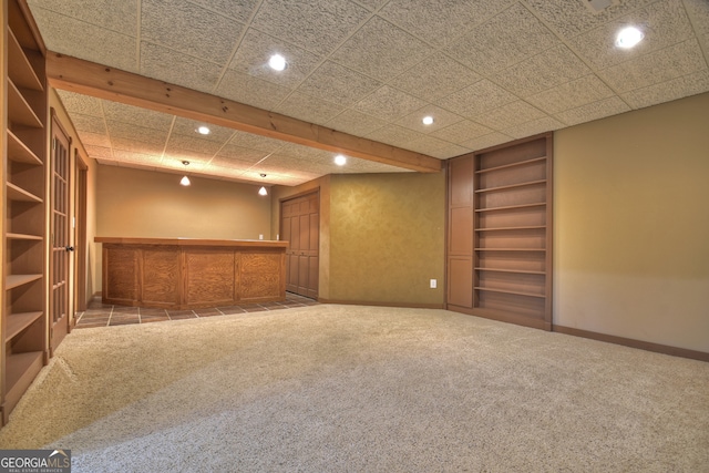 spare room with bar, built in shelves, carpet, and a drop ceiling