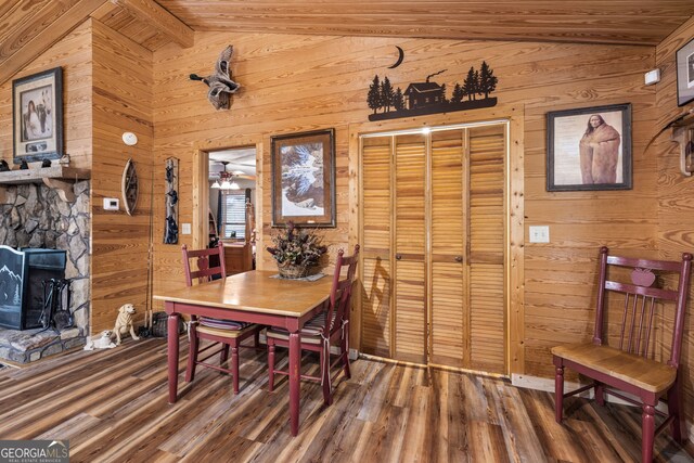 dining area featuring wooden walls, ceiling fan, a fireplace, vaulted ceiling, and dark wood-type flooring