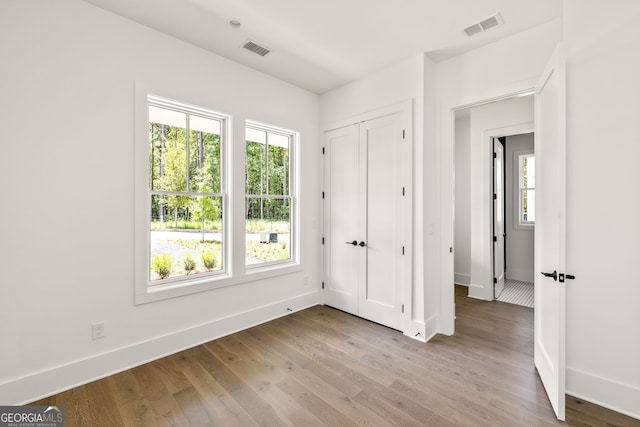 unfurnished bedroom featuring multiple windows, light hardwood / wood-style flooring, and a closet