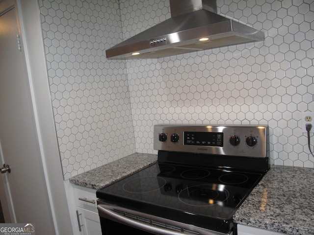 kitchen with white cabinetry, stainless steel range with electric cooktop, light stone countertops, backsplash, and wall chimney range hood