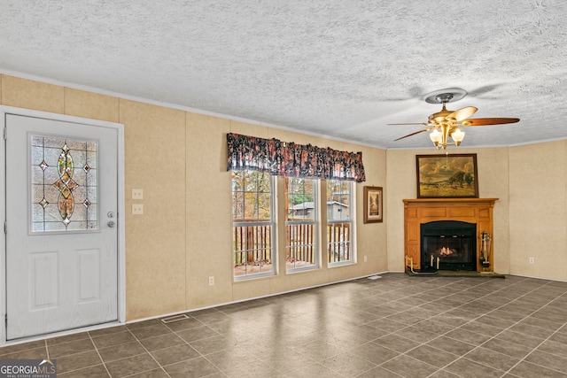 unfurnished living room with a textured ceiling, ornamental molding, dark tile flooring, and ceiling fan