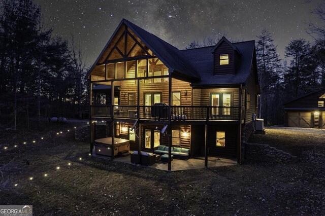 rear view of property with a garage, a patio area, a deck, an outbuilding, and a hot tub