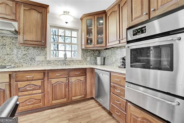 kitchen featuring light wood-type flooring, sink, decorative backsplash, light stone countertops, and appliances with stainless steel finishes