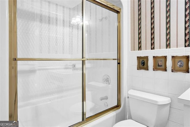 bathroom featuring bath / shower combo with glass door, tile walls, and toilet