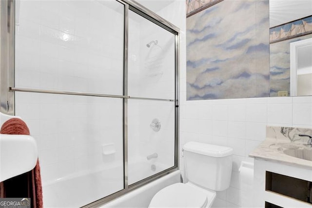 full bathroom with bath / shower combo with glass door, toilet, vanity, and tile walls