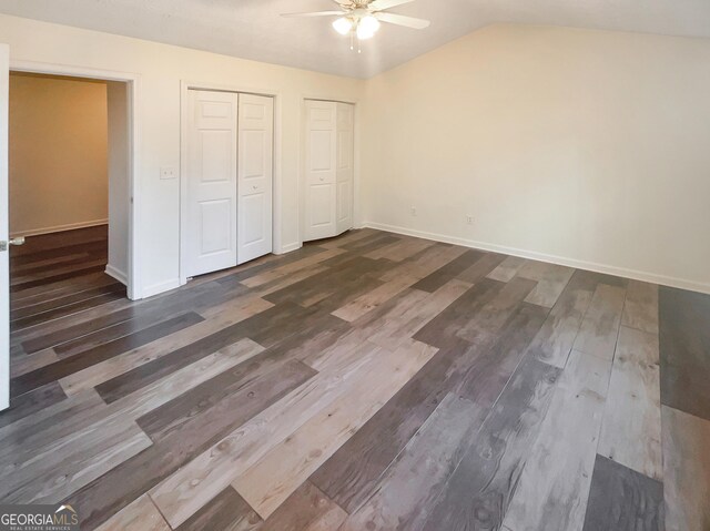 unfurnished bedroom featuring ceiling fan, vaulted ceiling, dark hardwood / wood-style flooring, and two closets