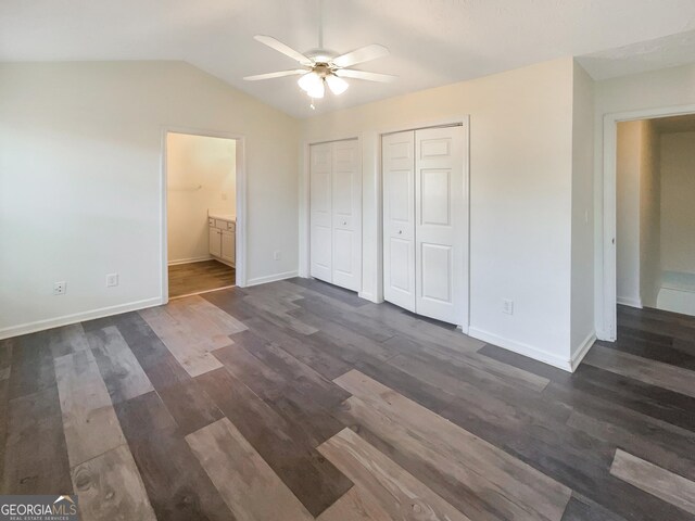 unfurnished bedroom featuring two closets, ceiling fan, dark wood-type flooring, connected bathroom, and lofted ceiling