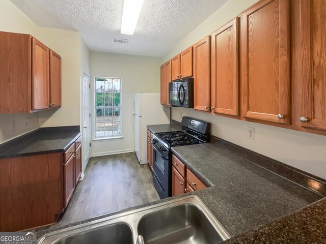 kitchen featuring dark hardwood / wood-style floors, sink, black appliances, and a textured ceiling