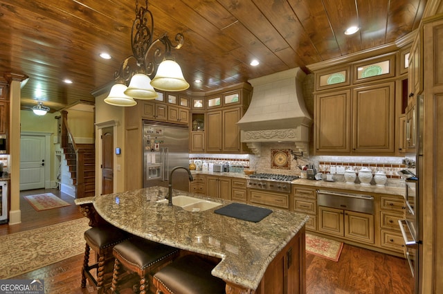 kitchen featuring custom exhaust hood, stainless steel appliances, sink, an island with sink, and dark wood-type flooring