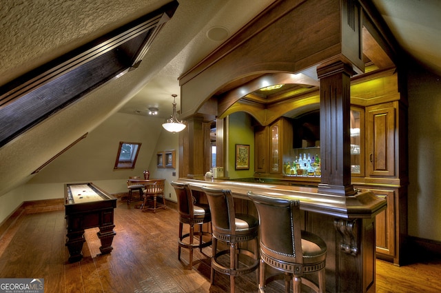 bar featuring decorative columns, hanging light fixtures, dark hardwood / wood-style flooring, and a textured ceiling