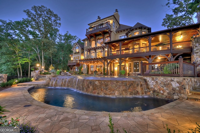 pool at night featuring a patio area and pool water feature