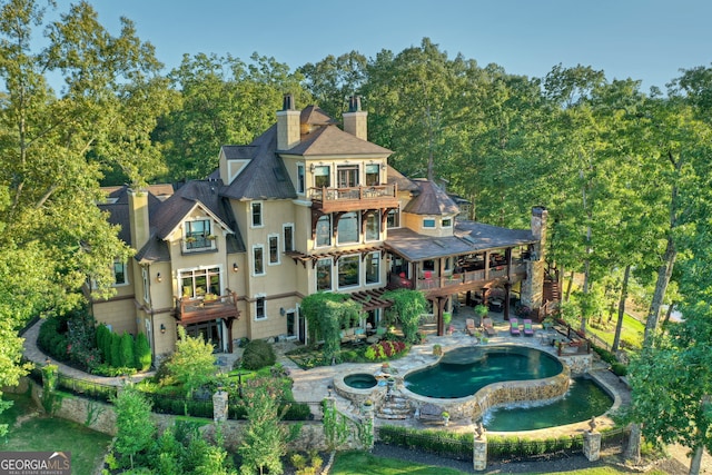 back of house with a balcony and an in ground hot tub