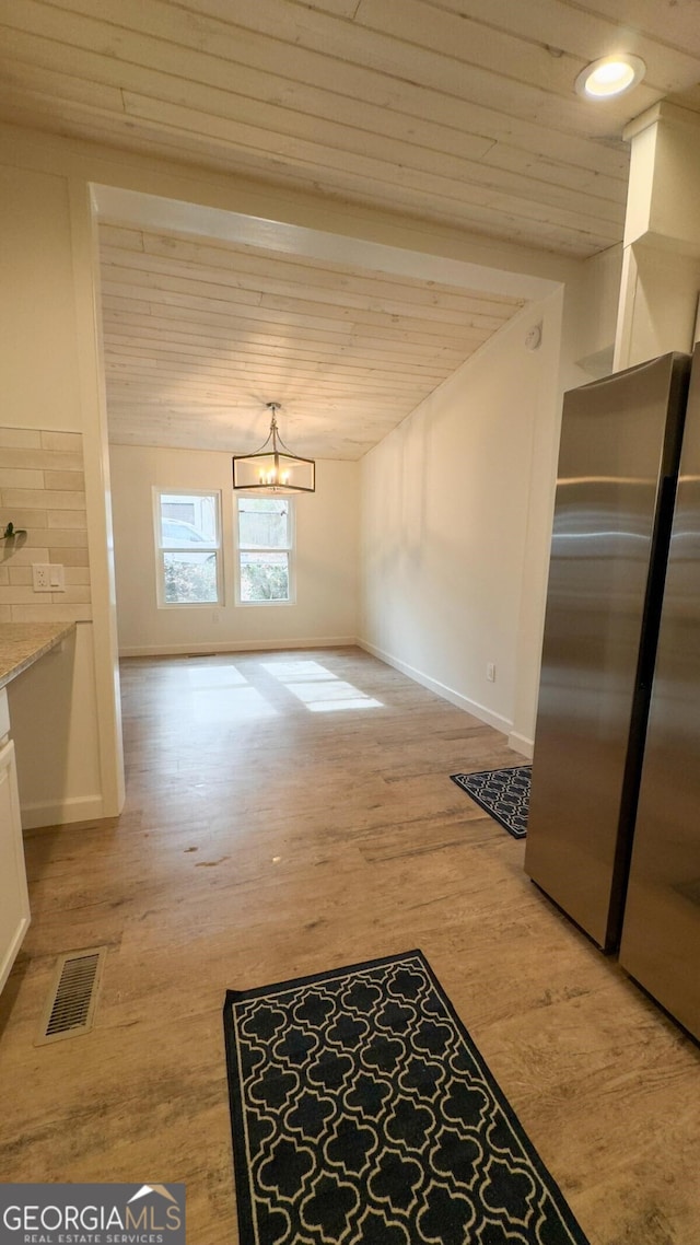 unfurnished dining area featuring beamed ceiling, a notable chandelier, and light wood-type flooring