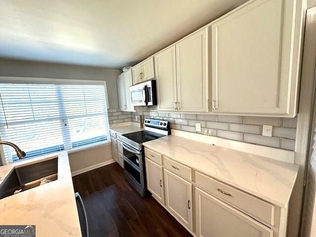 kitchen with appliances with stainless steel finishes, dark wood-type flooring, white cabinetry, sink, and light stone counters