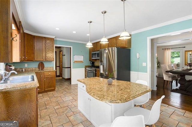 kitchen featuring a center island, sink, ornamental molding, appliances with stainless steel finishes, and decorative light fixtures